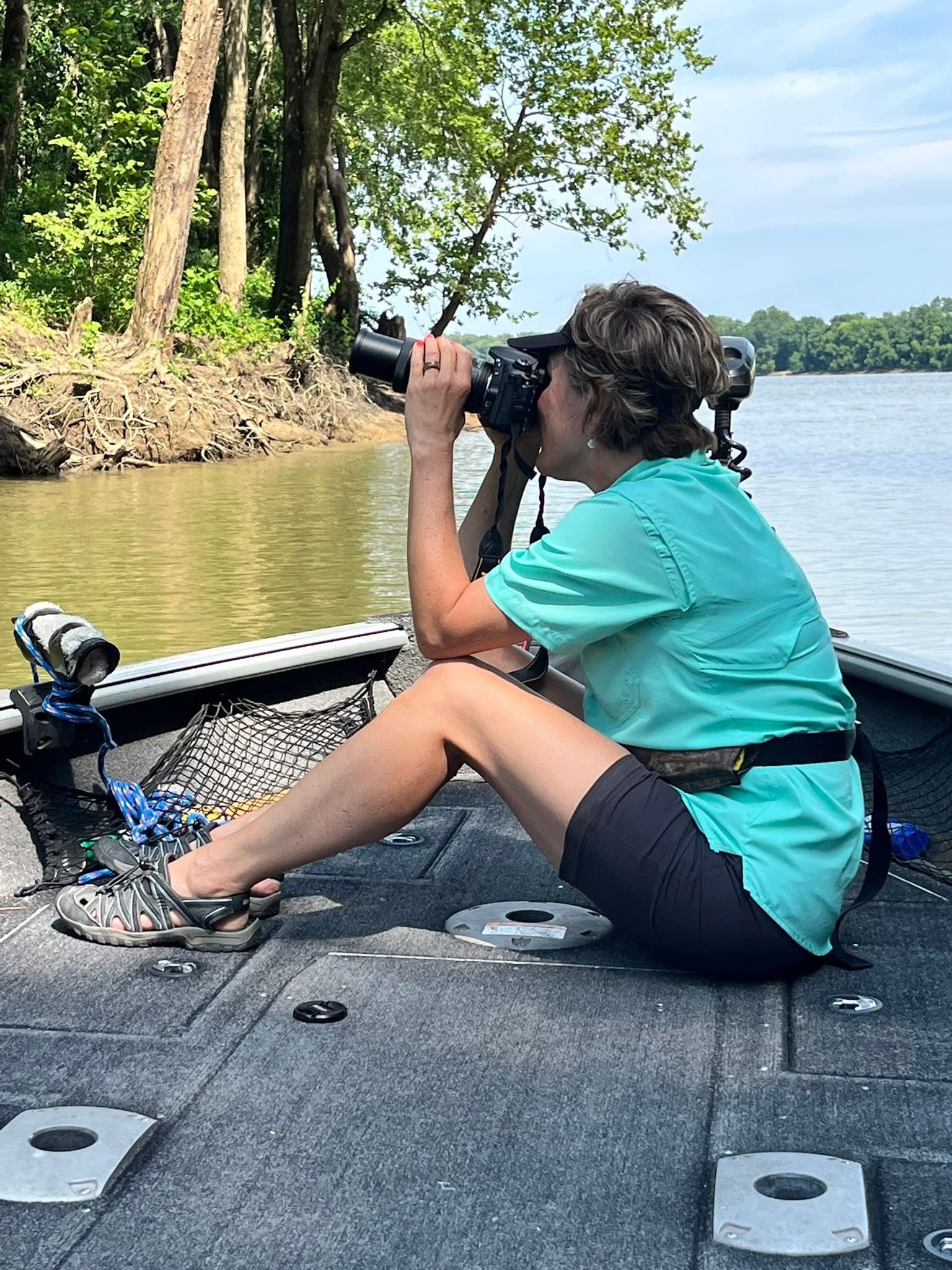 Image of the Wildlife Artist Lindsey Kiser capturing photographs of birds from the bow of a boat at the mouth of the Kentucky River in Carrollton, Kentucky.